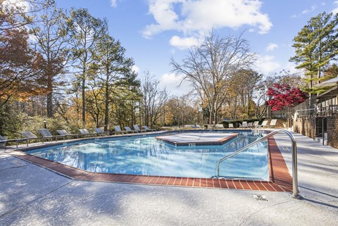 A pool surrounded by trees in a sunny day at Riverwood Crossing apartments in Roswell, GA.